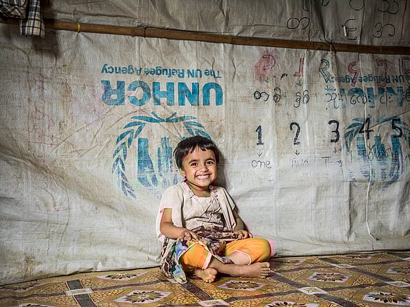 En liten flicka sitter i ett tält i Bangladesh.