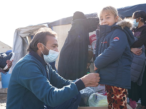 En hjälparbetare hjälper en flicka att ta på sig en jacka.