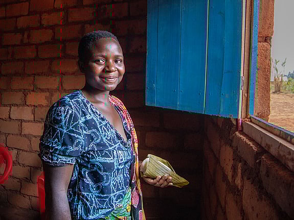 En kvinna står i ett rött tegelhus. Hon ler mot kameran.