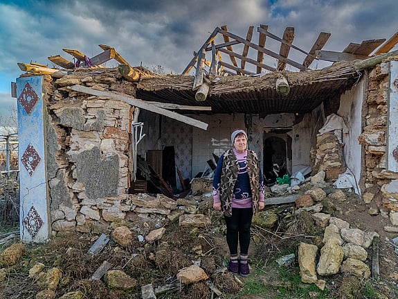 En ukrainsk kvinna står i rasmassorna av sitt eget hus. Hon tittar in i kameran.