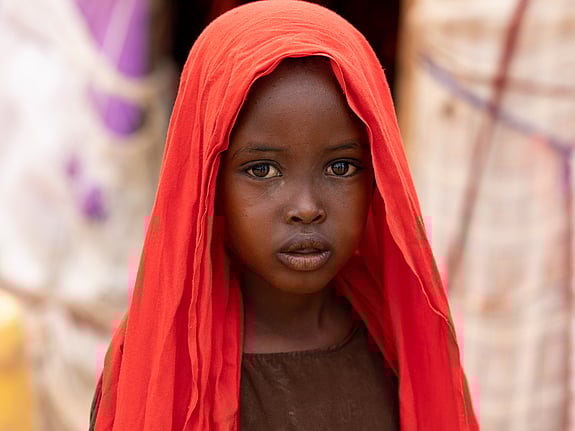 Ett barn på Afrikas Horn med röd sjal tittar in i kameran.