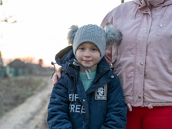 En familj i Ukraina står på en väg med sönderbombade hur.