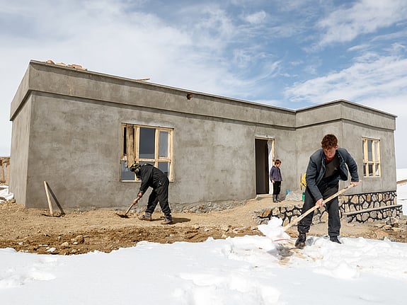 En familj röjer snö framför sitt nya hus i en bergsby i Afghanistan.