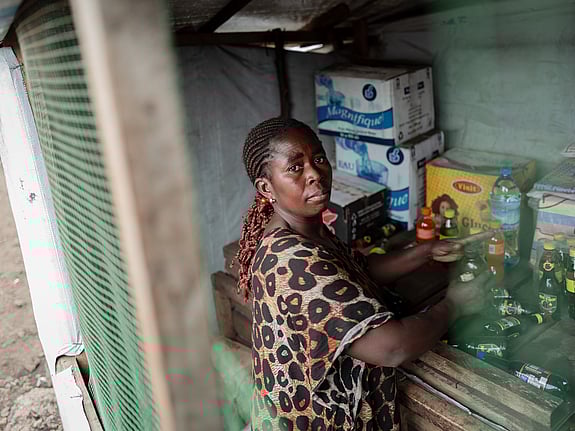 En kvinna står i sitt kök. Hon tittar allvarsamt mot kameran.