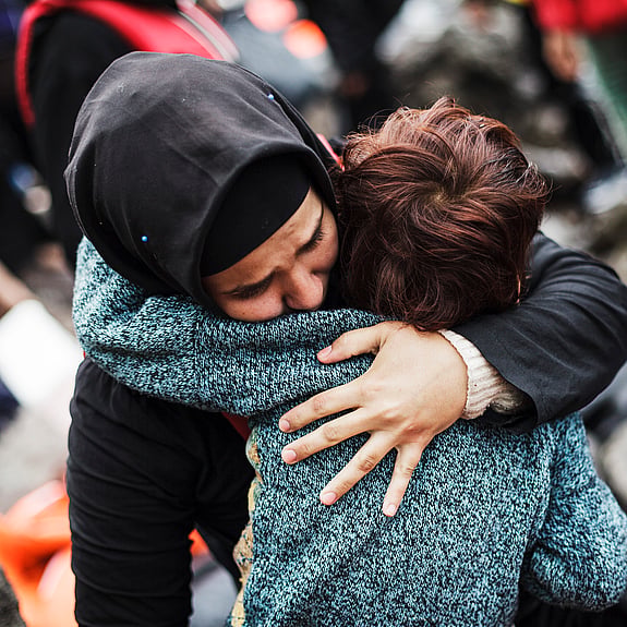 En syrisk flykting som korstat Egeiska havet från Turkiet i en ranglig båt kramar sin son efter att ha nått trygghet på ön Lesbos i Grekland.