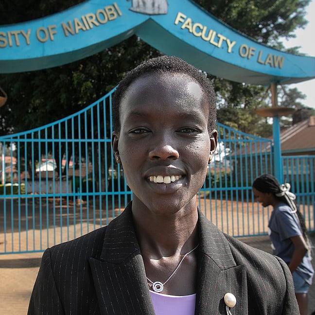 Monicah står framför ingången till skolan. Hon ser glad ut.