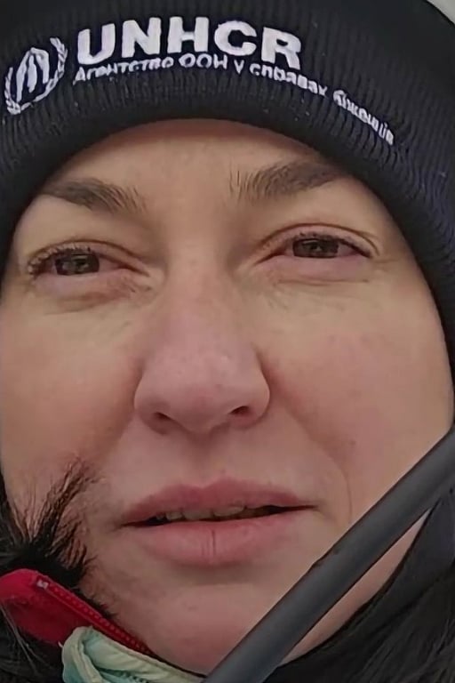 En kvinna med UNHCR-mössa står i vinterkläder framför en hjälpkonvoj i Ukraina.