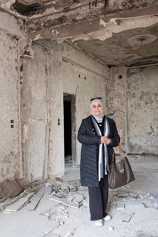 En kvinna står i ett sönderbombat hus.