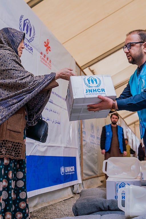 En UNHCR-medarbetare lämnar över en kartong med förnödenheter i Afghanistan.