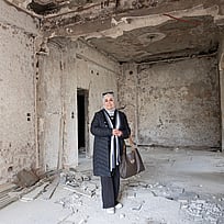 En kvinna står i ett sönderbombat hus.