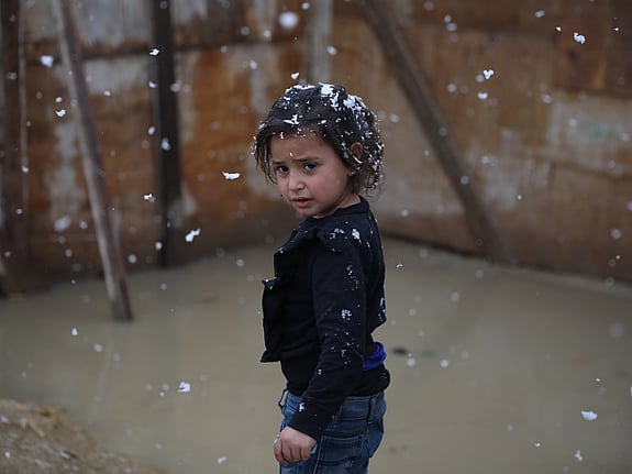 En liten flicka står utan jacka i snöslask.