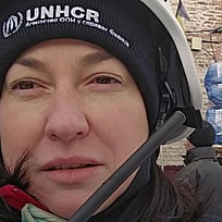 En kvinna med UNHCR-mössa står i vinterkläder framför en hjälpkonvoj i Ukraina.