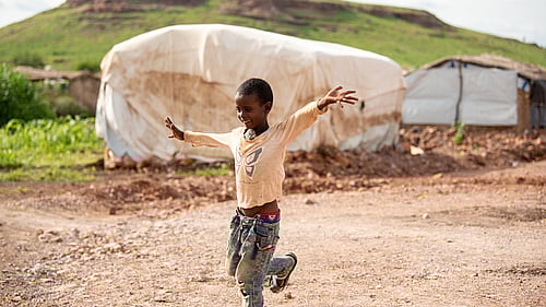 En pojke står på ett ben i ett flyktingläger. Han håller kursen.