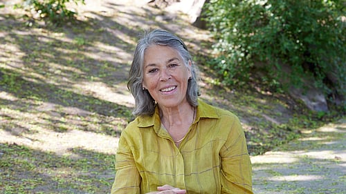 En kvinna sitter på marken och ler mot kameran.