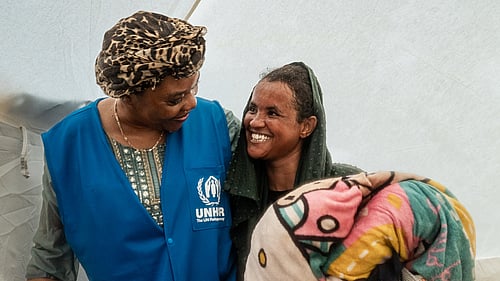 UNHCR-personal sitter på huk framför två barn i vinterkläder.