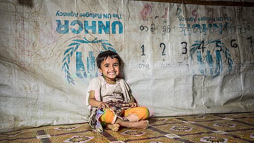 En liten flicka sitter i tält och skrattar.