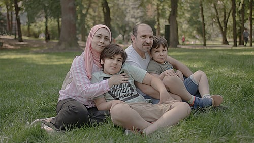 En familj på flykt från Syrien sitter i gräset.