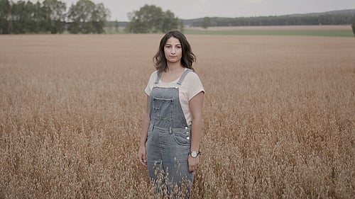 En kvinna står på ett fält med högt gräs.