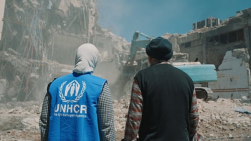 Två personer står och tittar på ett raserat hus.