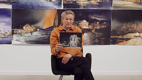 Lars Lerin sitter på en pall och visar upp en tavla.