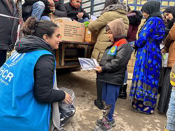 En UNHCR-medarbetare hjälper ett barn att ta på en jacka.