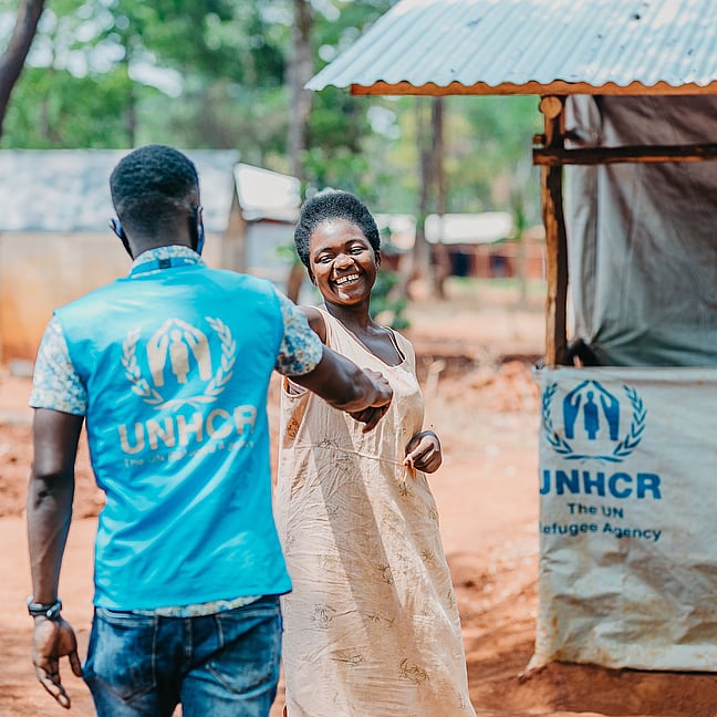 En fältarbetare på UNHCR och en kvinna hälsar glatt på varandra i ett flyktingläger. UNHCR skyddar människor på flykt i världen.