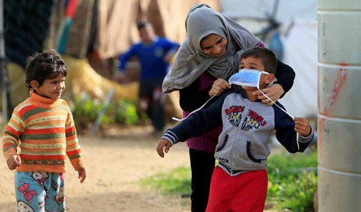 En syrisk mamma hjälper en pojke med munskydd i ett flyktingläger i Libanon. 