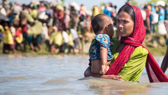 En mamma flyr med sin bebis över ett översvämmat fält på gränsen mellan Myanmar och Bangladesh.