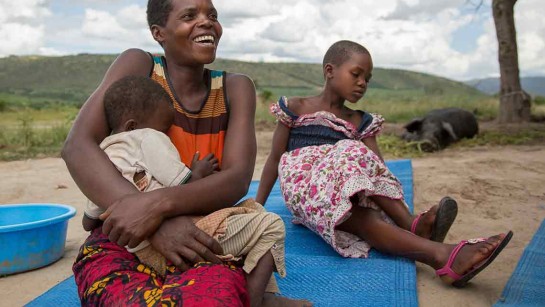 Janine sitter med sina två barn och utanför deras hem i Oruchinga-lägret i västra Uganda. 