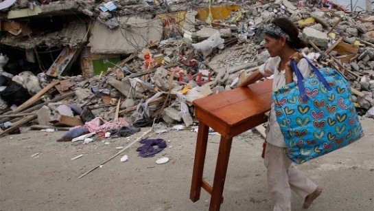 En kvinna bär ett bord genom gatorna i jordbävningsdrabbade Pedernales i Ecuador. Hela söndagen letade räddningsarbetare överlevande i rasmassorna. 