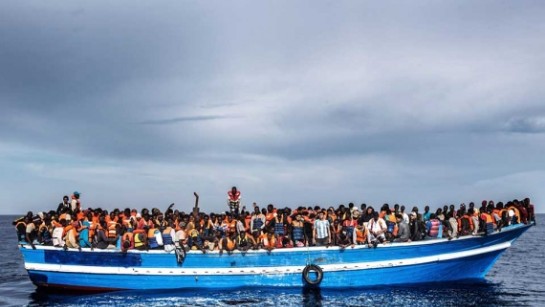 En båt med flyktingar och migranter utanför Italiens kust sedd från en räddningsbåt, juni 2014. 
