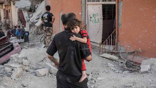 En litet barn håller sig fast i en man när de flyr från strider i Mosul. En litet barn håller sig fast i en man när de flyr från strider i Mosul. 