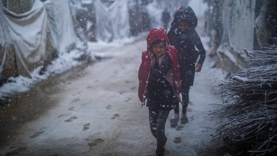 Flickor på flykt från Syrien vandrar genom ett tältläger i Libanon mitt i ett snöoväder.