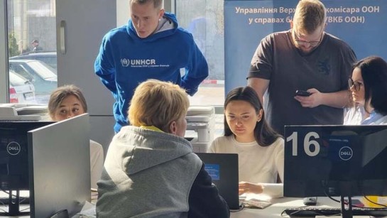 Kollegor i Ukraina hjälper en kvinna på flykt registrera sig för kontantstöd.