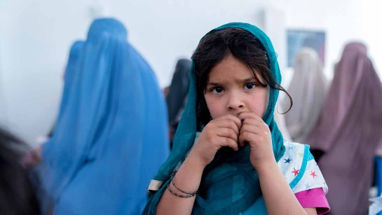 En flicka väntar på att sin äldre syster ska få ett kontantstöd från UNHCR i ett läger norr om Kandahar.