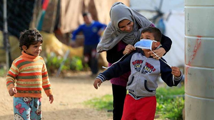 En syrisk mamma hjälper en pojke med munskydd i ett flyktingläger i Libanon. 